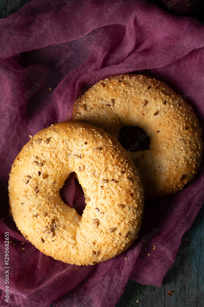 Homemade large bagels with sesame and sunflower seeds on burgundy gauze, top view