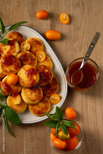 Delicious homemade pancakes with cottage cheese, kumquat jam and fruits on a wooden table, top view