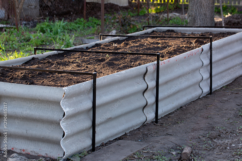 Permaculture raised warm bed made of slate with branches at the base in the garden