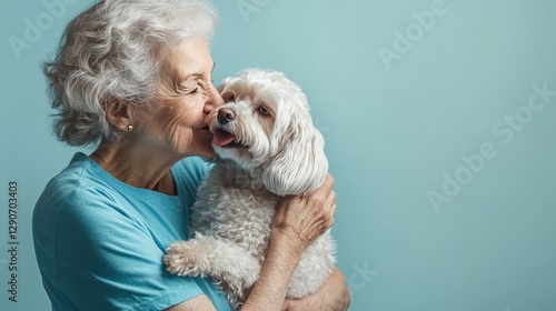 Photograph of an elderly woman in a blue t-shirt, holding and kissing her long-haired white dog against a light-blue background.
