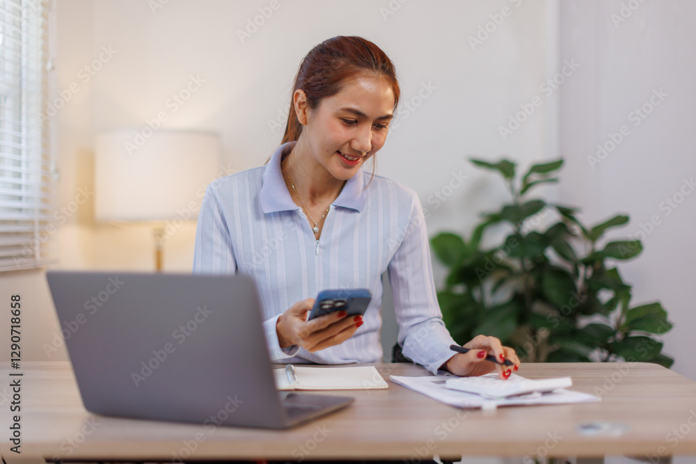 Serious charming asian woman using smartphone while working with laptop at home workplace.
Serious charming asian woman using smartphone while working with laptop at home workplace.