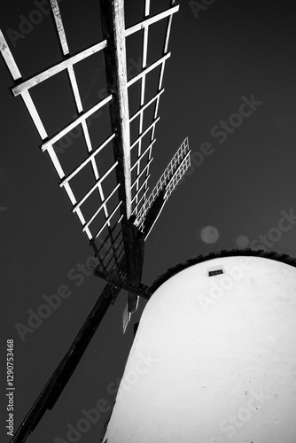 Fotografía en blanco y negro de un molino de viento capturado desde una perspectiva baja, resaltando la imponencia de sus aspas contra el cielo. La imagen enfatiza la textura y el contraste 