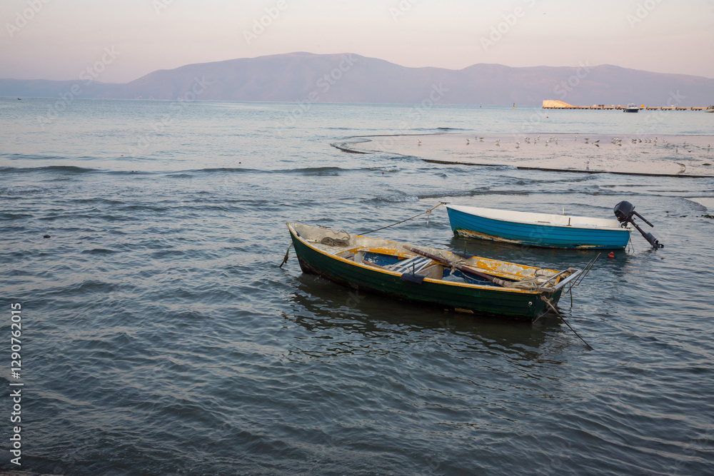 Naklejka premium Boats quietly bobbing on calm waters at sunset near a mountainous landscape