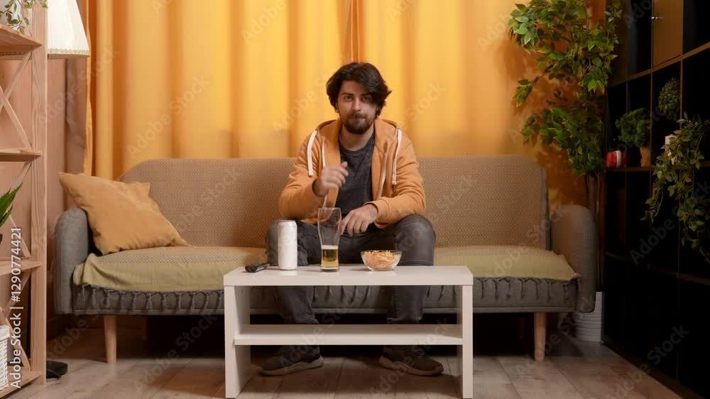 A man sitting on the sofa in the room, watching TV and cheering for a sports team. A man sitting on the sofa in the room, watching TV and cheering for a sports team.