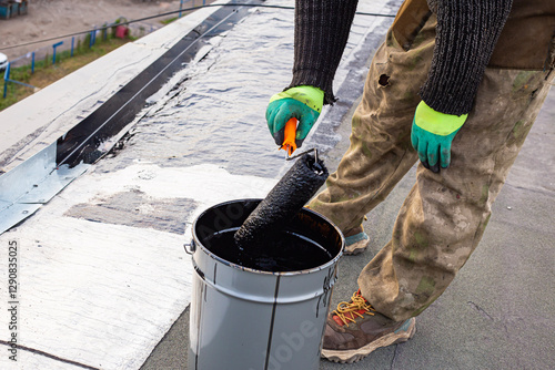 Fényképezés a young worker treats a roof with bitumen primer before applying rolled asphalt