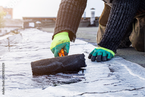 a young worker treats a roof with bitumen primer before applying rolled asphalt roofing using a torch