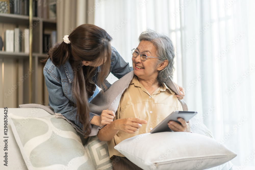 Obraz premium Asian senior mother and daughter smiling and talking using tablet browsing social media, shopping online, watching movies or series, enjoying entertainment digital connection and bonding at home