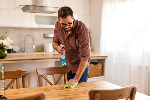 Wallpaper Mural A man is cleaning a table at home, wiping down the surface to maintain a clean and organized space. The image captures a moment of home upkeep and attention to cleanliness in a cozy, everyday setting. Torontodigital.ca