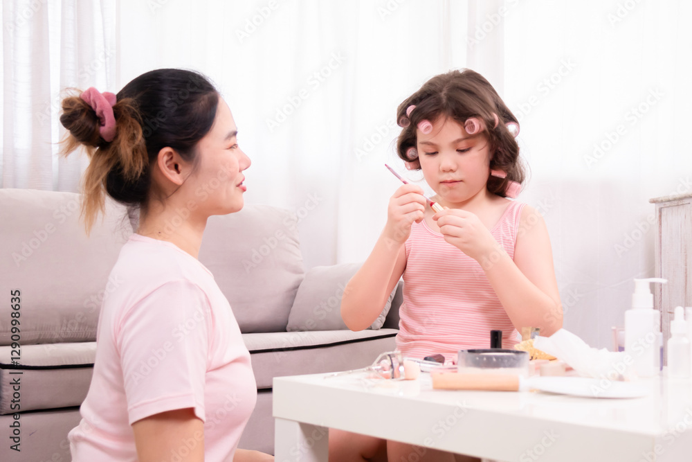 Cheerful young girl with pink curlers in her hair shares loving moment with her mother, enjoying fun and affectionate beauty routine at home. Take turns applying makeup, family warmth, spending time. Cheerful young girl with pink curlers in her hair shares loving moment with her mother, enjoying fun and affectionate beauty routine at home. Take turns applying makeup, family warmth, spending time.