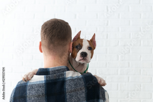 Man with dog over shoulder against a white brick wall