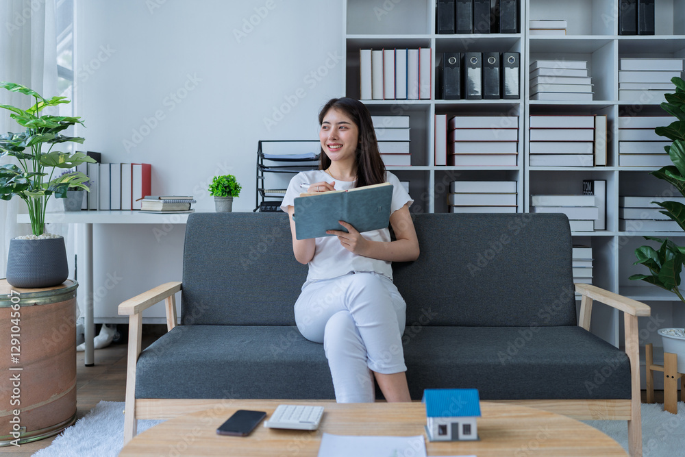 Young woman analyzing financial documents at home with calculator and model house on table in modern living room Young woman analyzing financial documents at home with calculator and model house on table in modern living room