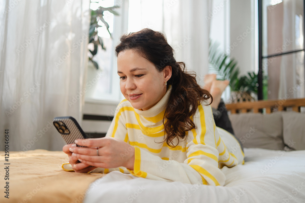 Woman Relaxing on Bed Using Smartphone in Cozy Bedroom at Home Woman Relaxing on Bed Using Smartphone in Cozy Bedroom at Home