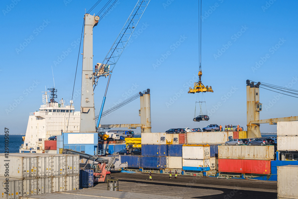 Port crane loading car into containers on bull carrier in port on