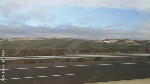View from a bus window traveling to Girona on an autumn day, Spain. Video 31 seconds. Rolling hills, fields, and villages pass by under a partly cloudy sky