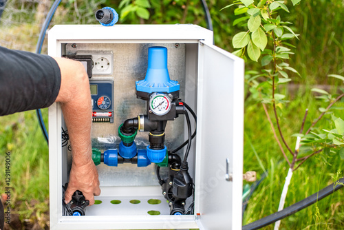 Installation of a drip irrigation system. A man installs an Automatic Water Supply Regulation System in a metal box
