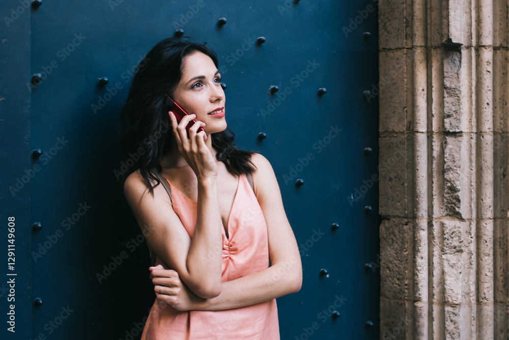 Fototapeta premium Dreamy woman speaking on smartphone outside old building