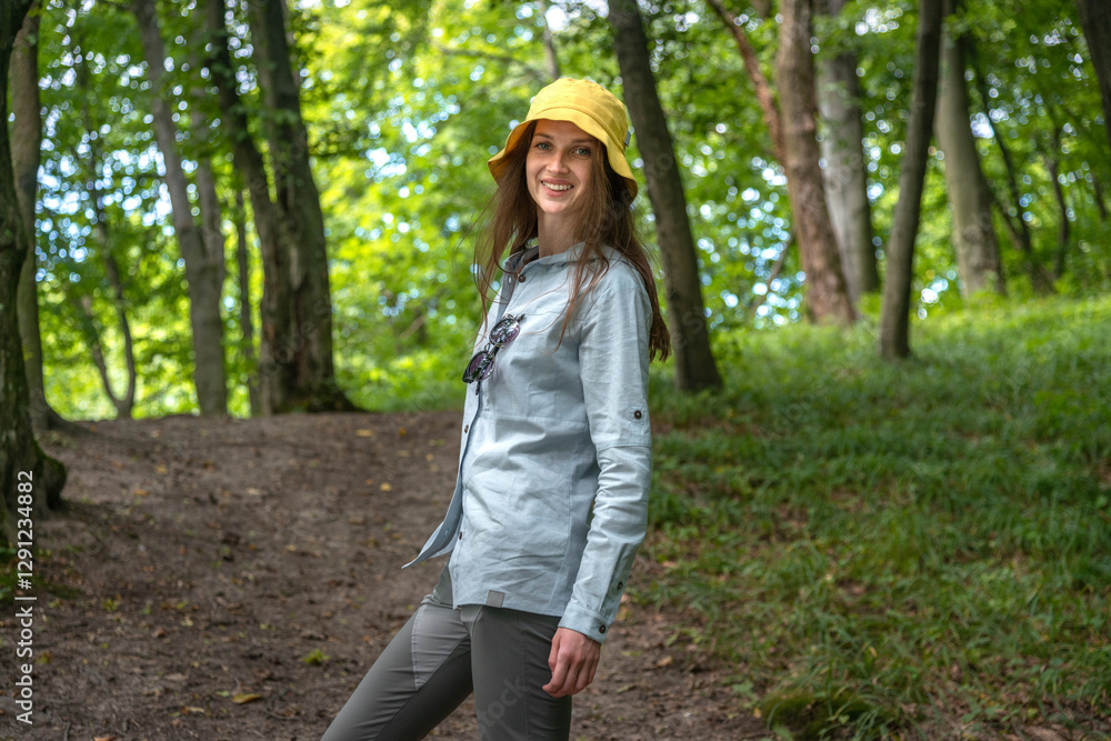 Candid shot of a female hiker standing confidently in a forested mountain area, with backpack, surrounded by lush green trees and dappled sunlight. Candid shot of a female hiker standing confidently in a forested mountain area, with backpack, surrounded by lush green trees and dappled sunlight.
