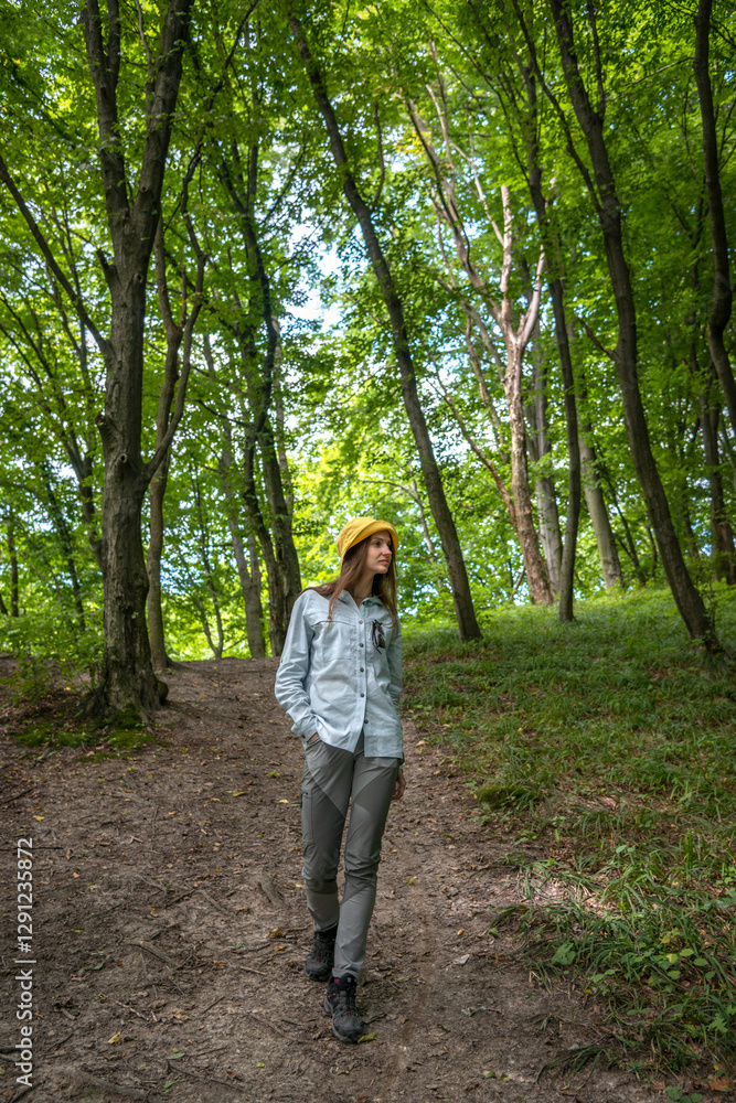 A female hiker walking confidently in a forested mountain area, wearing a hat and backpack, surrounded by lush green trees and dappled sunlight. A female hiker walking confidently in a forested mountain area, wearing a hat and backpack, surrounded by lush green trees and dappled sunlight.