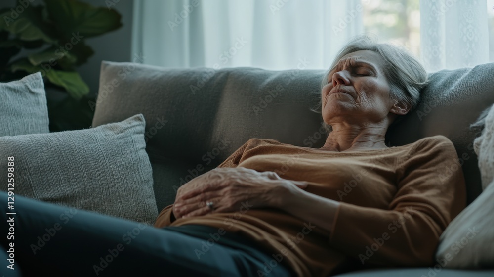 Abdominal pain causing a senior woman to lie on the couch, clutching her stomach. Featuring discomfort and worry Abdominal pain causing a senior woman to lie on the couch, clutching her stomach. Featuring discomfort and worry