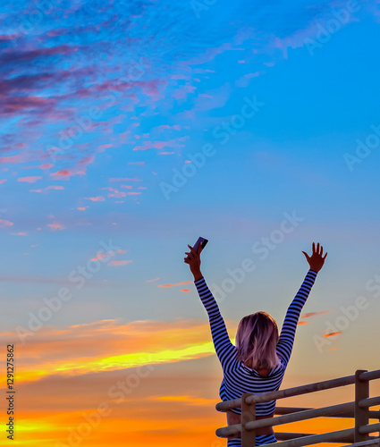 Silhouette of happy young woman on balcony at early morning during colorful s...