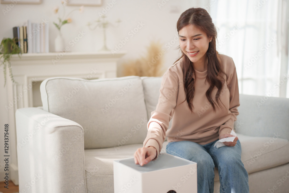 Healthy Asian woman smiles as she adjusts the settings on an air purifier placed beside her. Healthy Asian woman smiles as she adjusts the settings on an air purifier placed beside her.