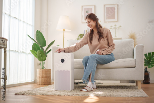 Healthy Asian woman is operating an air purifier while relaxing at home, enjoying a moment of tranquility.