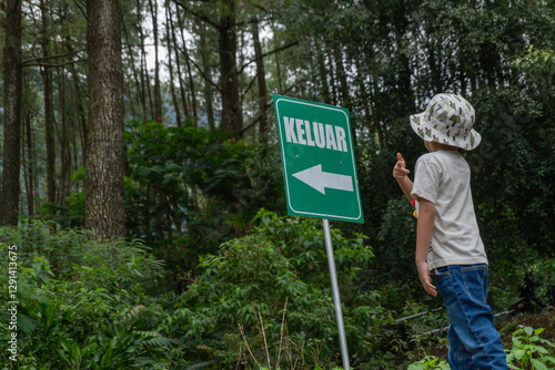 A young boy wearing a bucket hat and casual clothes looking for a sign that say 