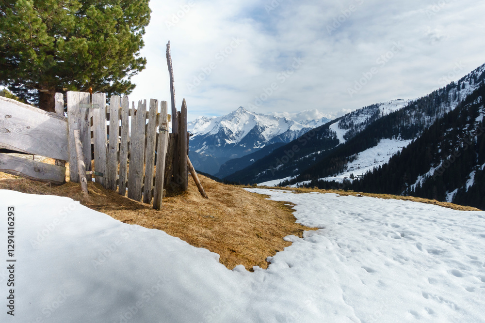 Holzgatter mit Schneeresten und Berg im Hintergrund