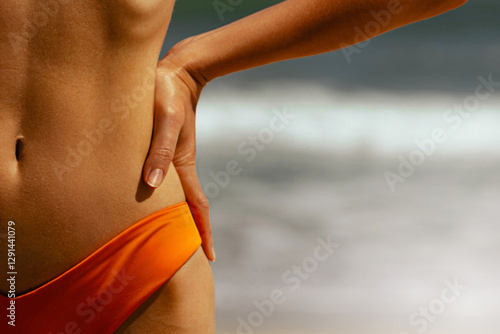 Fototapeta Female in orange swimwear standing by ocean