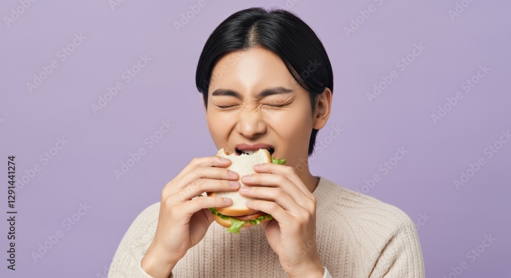 Asian young adult male enjoying a sandwich against light purple background Asian young adult male enjoying a sandwich against light purple background