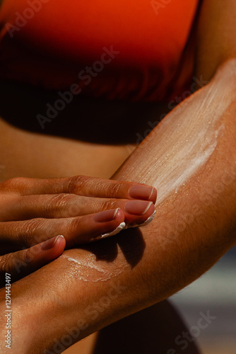 Young hispanic female applying sunscreen on arm at beach. Skin care, sun protection