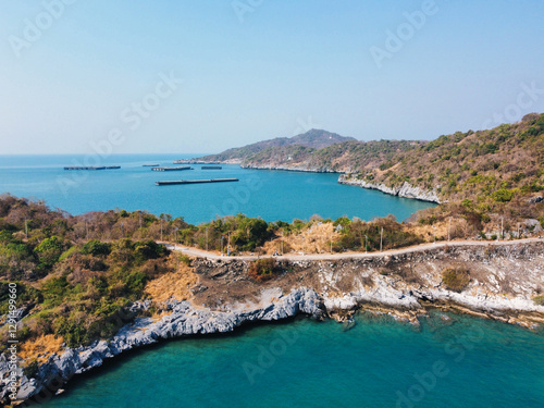 Aerial view of a picturesque coastal road meandering through vibrant foliage, overlooking the turquoise waters and rocky shoreline of the Ko Sichang Thai island in Chonburi photo