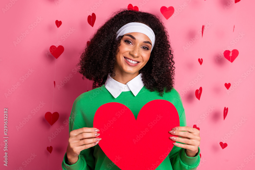 Smiling woman in green sweater with red heart on pink Valentine's background Smiling woman in green sweater with red heart on pink Valentine's background