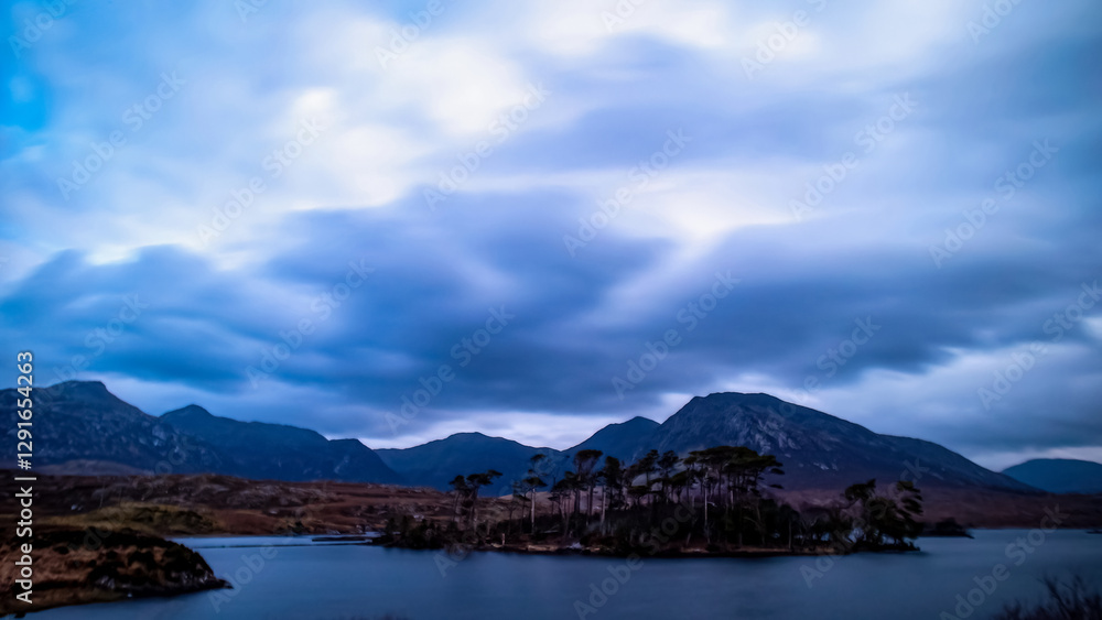 Blue hour at Pine Island under cloudy full moonlight, with the Twelve Bens in the background, Connemara, Ireland. Blue hour at Pine Island under cloudy full moonlight, with the Twelve Bens in the background, Connemara, Ireland.