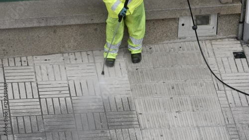 Street cleaner is using a pressure washer to clean a city sidewalk