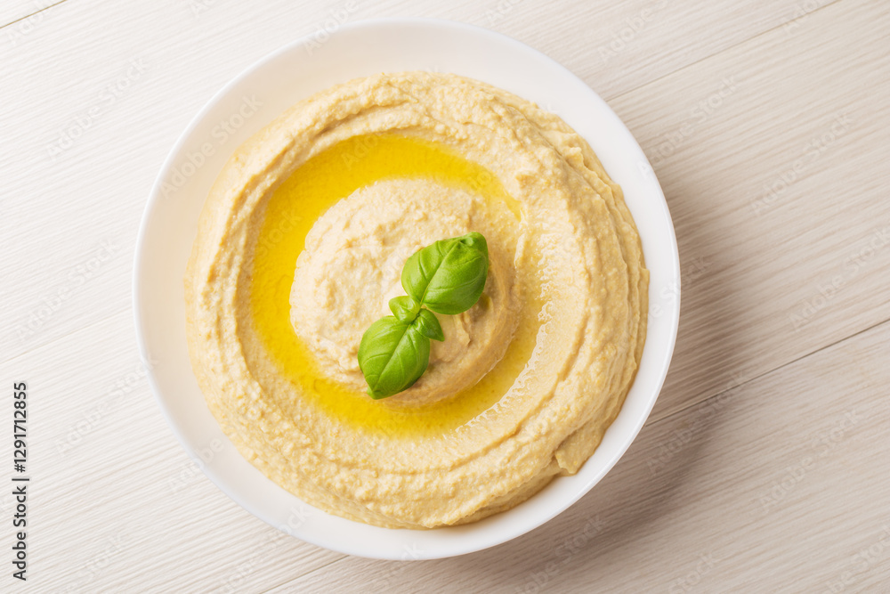 Top view on homemade hummus with olive oil in a white bowl on a light wooden background. Traditional Arabic snack. Top view on homemade hummus with olive oil in a white bowl on a light wooden background. Traditional Arabic snack.