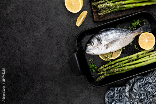 the concept of a delicious dinner. raw dorado fish with asparagus and lemon on dark background.