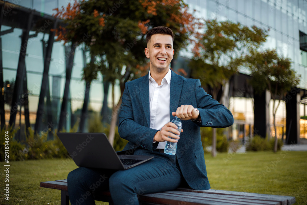 Fototapeta premium Man Sitting on Bench with Laptop and holding a bottle of water