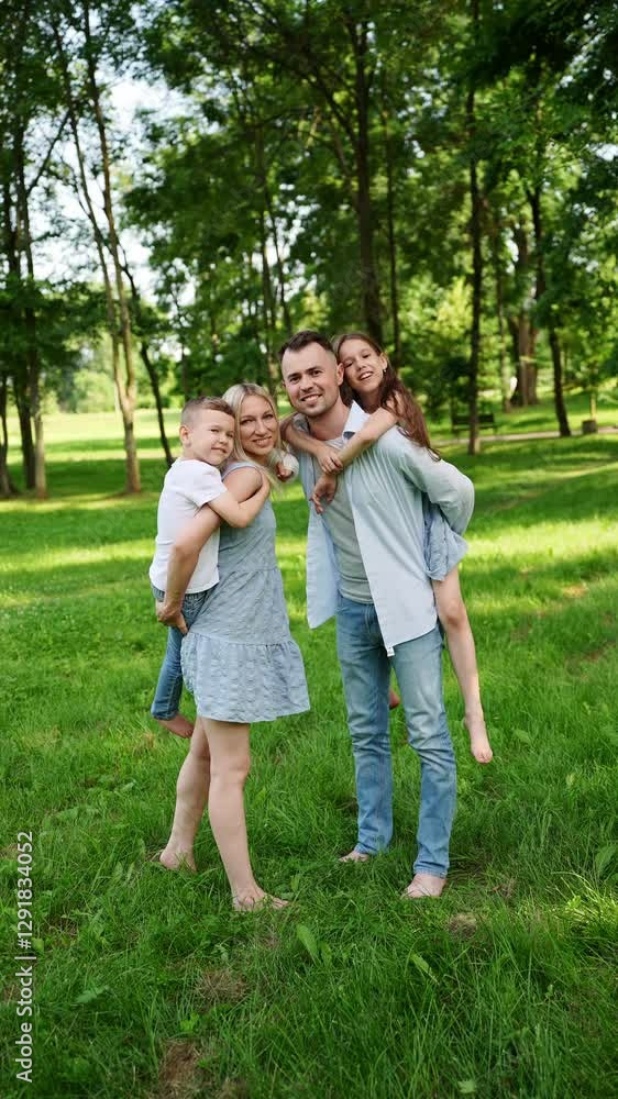 Happy family in nature. Mom and dad standing next to each other holding cute boy and girl on shoulders, smiling happily, showing unity, love, spending leisure time together. Parenthood, guardianship