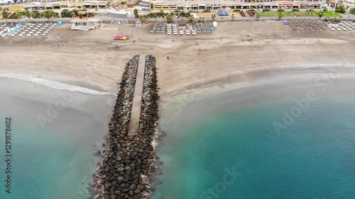 Aerial view of Costa Adeje city beach, Tenerife, Canary islands. Cinematic 4K footage with sandy sea shore, Atlantic ocean coast, waves, quay with people walking. Bird-eye video, lateral movement shot