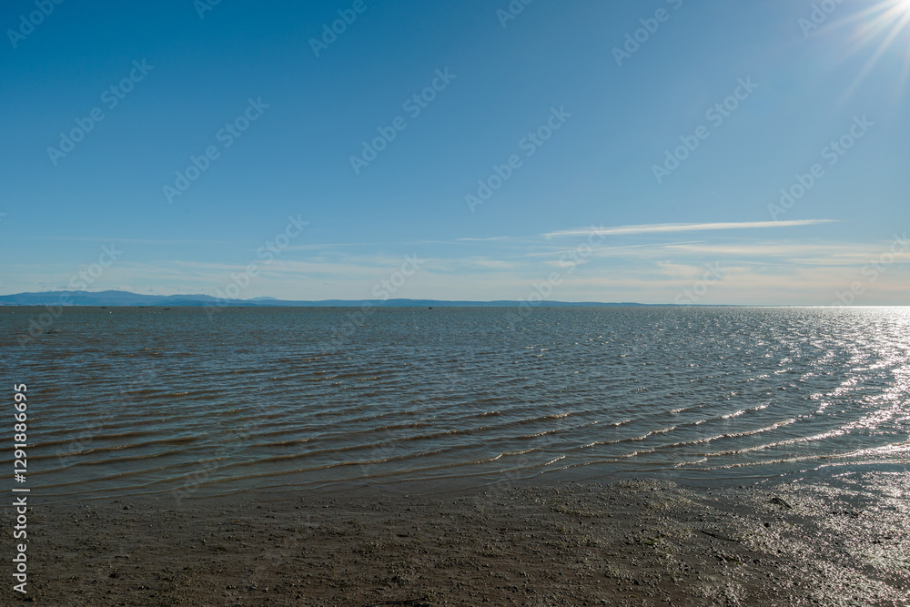 vista che si estende sull'area marina del Golfo di Trieste, nel mare Adriatico, guardando verso le colline e le montagne distanti tra Italia e Slovenia, di giorno, con cielo sereno, in inverno