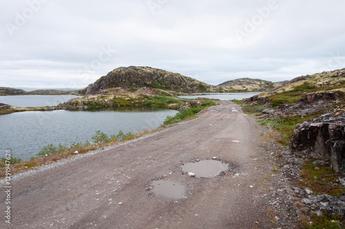 Country road among rocks and lakes in tundra. Cloudy summer day. Murmansk region, Russia