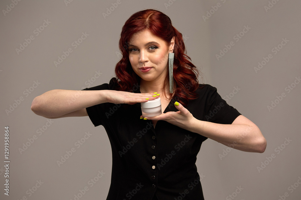 Elegant woman with red hair holding cosmetic jar, neat nails, stylish earrings, cream, beauty product showcase concept