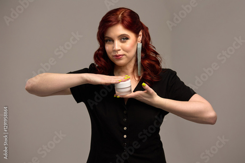 Obraz na płótnie Elegant woman with red hair holding cosmetic jar, neat nails, stylish earrings, cream, beauty product showcase concept w salonie