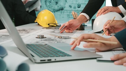 A group of engineers engages in a detailed planning session around blueprints and technical drawings, using laptops, tools, and safety gear, representing teamwork and innovation. SACTR