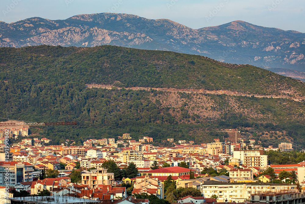 A breathtaking view of the bustling city of Budva set against a backdrop of lush mountains at sunset.