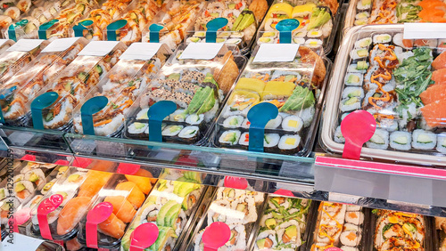 Sushi in a refrigerated display case in a sushi store, a variety of rolls, nigiri and sashimi with fresh salmon, avocado, shrimp and other ingredients, Japanese cuisine, perfect for takeaway or on-the