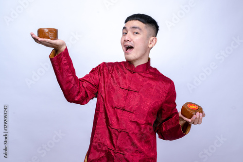 An Asian man in a red traditional Chinese Tang suit smiles while holding of traditional Chinese New Year cake (nian gao), symbolizing prosperity isolated against a plain white background. photo