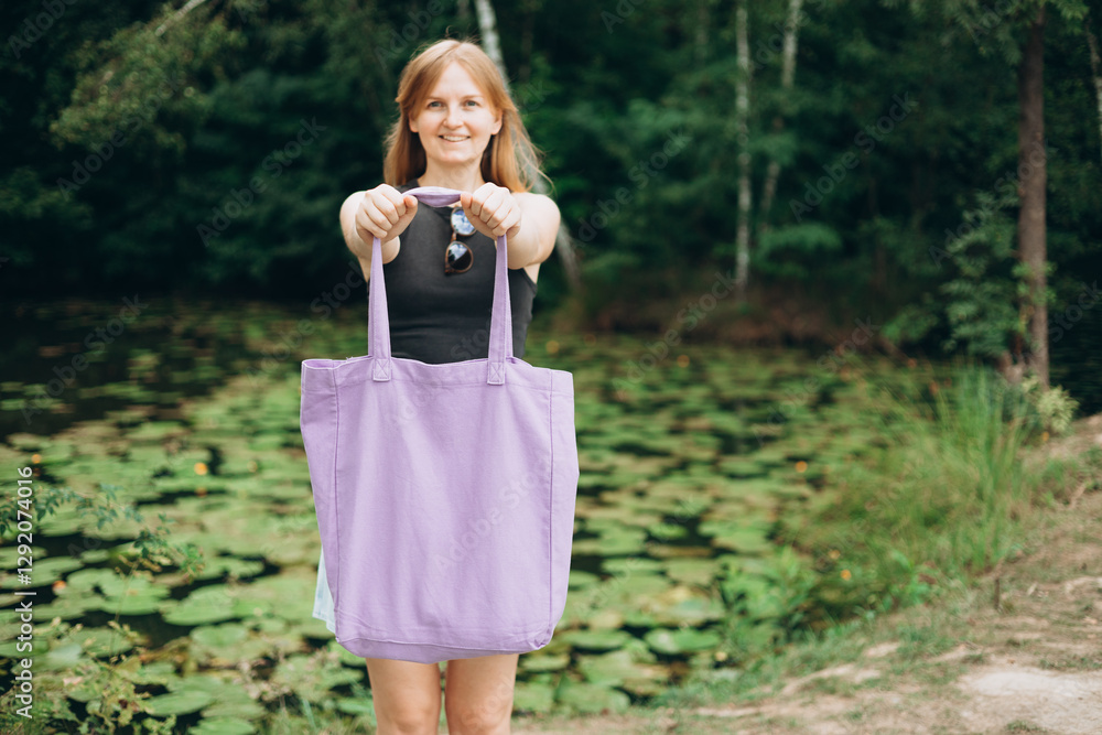 Young woman with canvas eco shopping bag on nature background. 30s woman is posing in a botanical garden with water lilies. Mockup, for logo