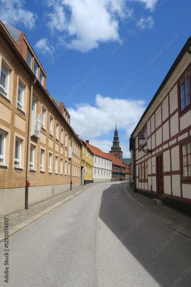 Hinter den Häusern dieser kurvigen Altstadtstraße in Ystad in Südschweden ist der Turm der St.-Maria-Kirche zu sehen. Es ist ein sonniger Sommertag. Hinter den Häusern dieser kurvigen Altstadtstraße in Ystad in Südschweden ist der Turm der St.-Maria-Kirche zu sehen. Es ist ein sonniger Sommertag.